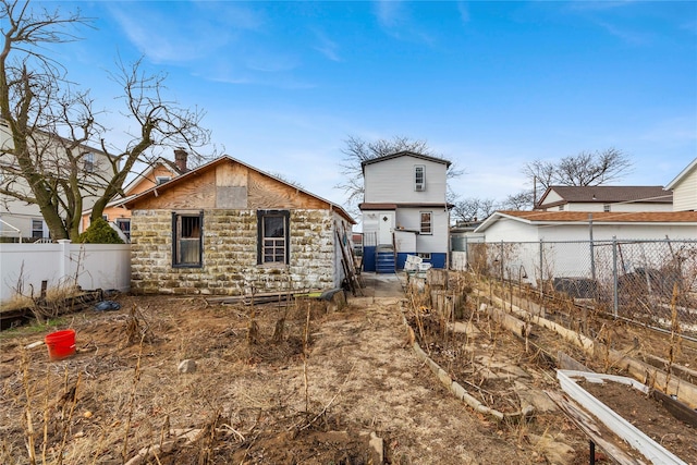 back of property with stone siding, a fenced backyard, and a chimney