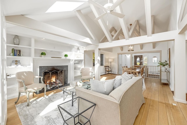 living room with built in shelves, a lit fireplace, light wood-style flooring, and a ceiling fan