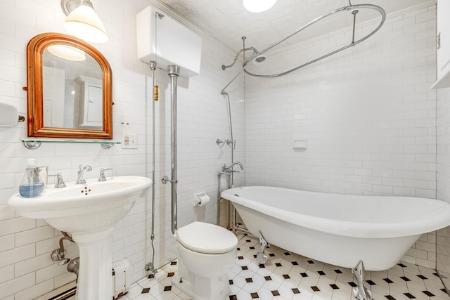 bathroom featuring a sink, tile walls, toilet, and a freestanding bath