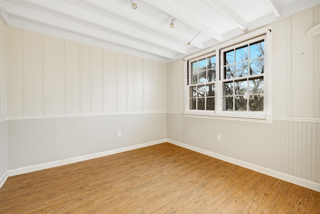 empty room with beamed ceiling, a healthy amount of sunlight, baseboards, and light wood-style floors