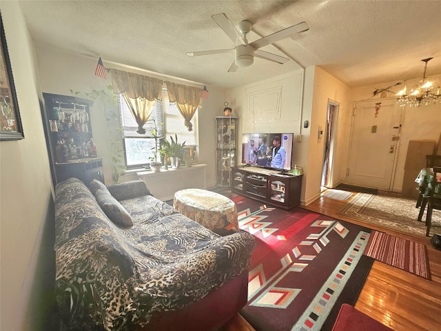 living room featuring a textured ceiling, wood finished floors, and ceiling fan with notable chandelier