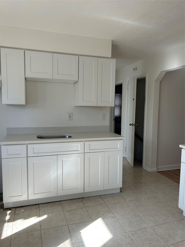 kitchen with light tile patterned floors, light countertops, a sink, and white cabinets