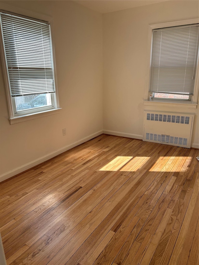 empty room featuring radiator heating unit, light wood-style flooring, and baseboards