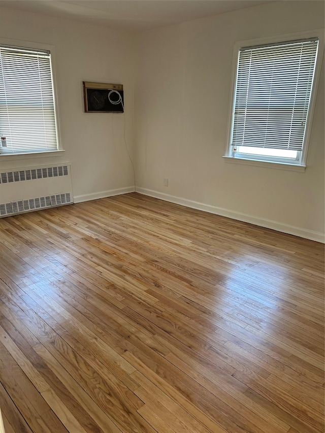 spare room with radiator heating unit, light wood-style flooring, and baseboards