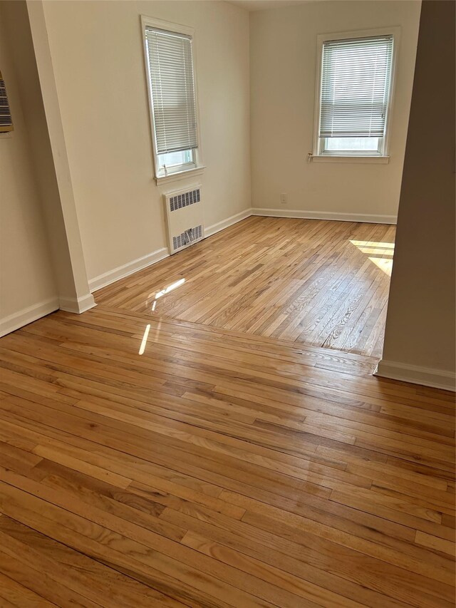 empty room featuring radiator, light wood-style floors, and baseboards