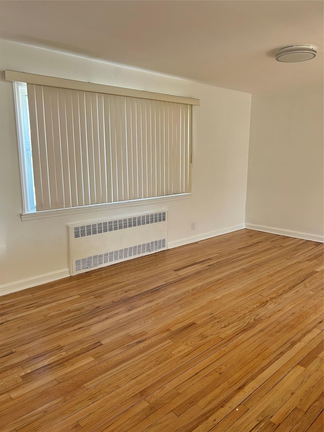 unfurnished room with radiator heating unit, light wood-type flooring, and baseboards