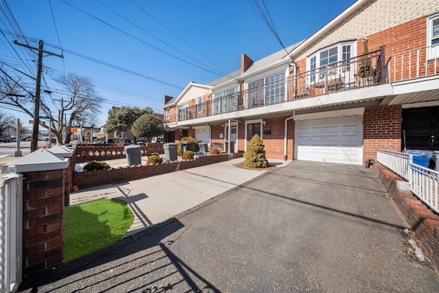 view of front facade with an attached garage, a chimney, aphalt driveway, and brick siding