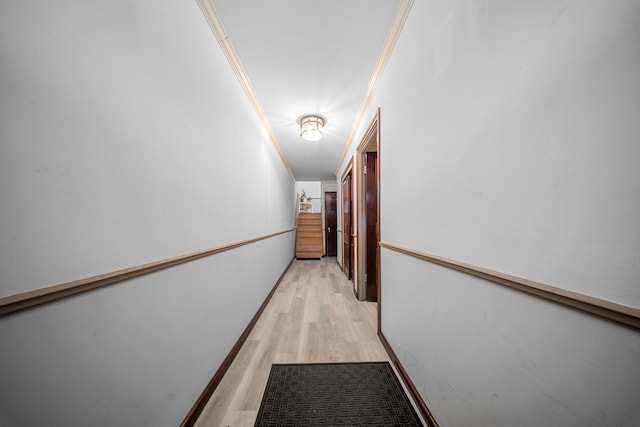 hallway featuring crown molding, light wood-style flooring, and baseboards