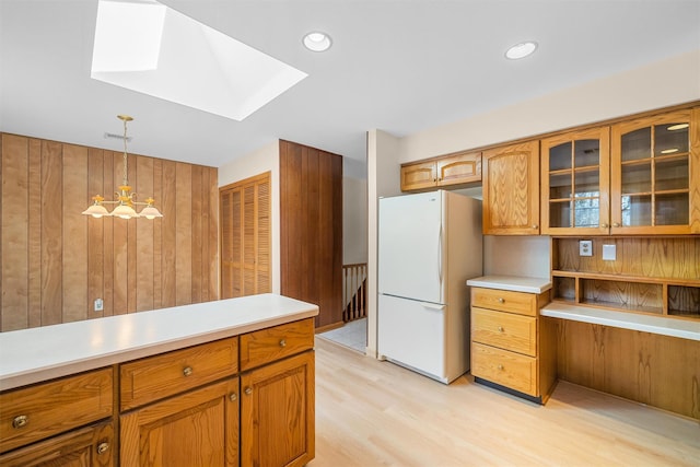 kitchen featuring decorative light fixtures, light countertops, freestanding refrigerator, brown cabinets, and glass insert cabinets