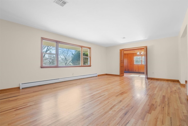 empty room with light wood finished floors, a baseboard radiator, visible vents, and baseboards