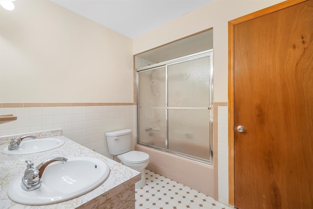 bathroom with toilet, shower / bath combination with glass door, a sink, and tile walls