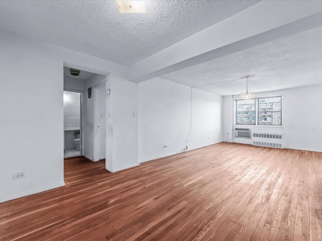 empty room featuring a chandelier, radiator, wood-type flooring, and a textured ceiling