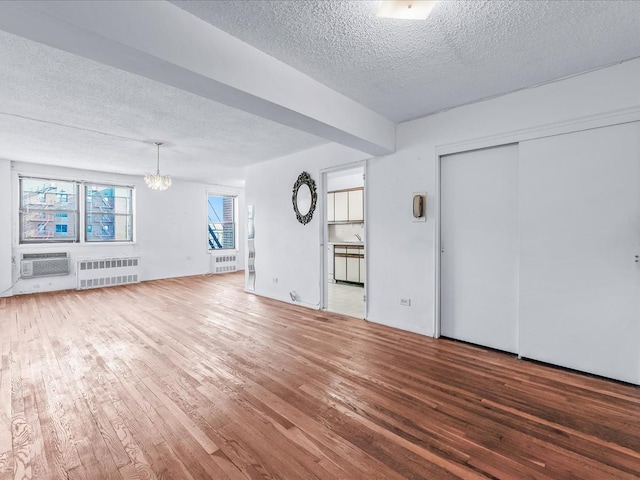 unfurnished living room with a textured ceiling, radiator heating unit, wood finished floors, and a wall mounted AC