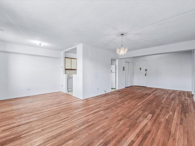 unfurnished living room featuring an inviting chandelier, light wood-style flooring, and a textured ceiling