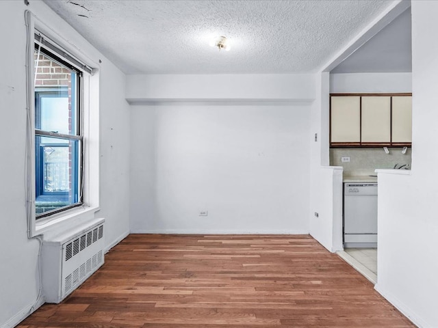 unfurnished room featuring baseboards, light wood-style flooring, radiator heating unit, and a textured ceiling