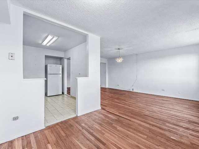 spare room featuring light wood-type flooring, a textured ceiling, and a notable chandelier