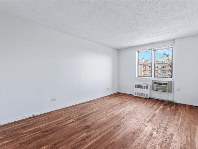 empty room with a textured ceiling, a wall unit AC, hardwood / wood-style flooring, and radiator