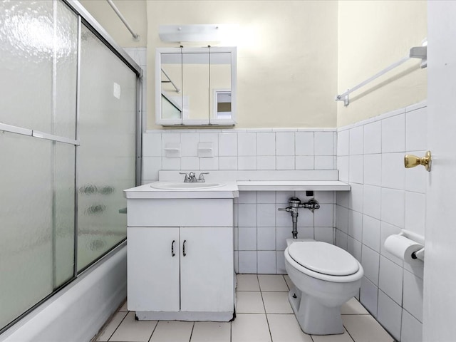 full bathroom with toilet, tile patterned floors, combined bath / shower with glass door, vanity, and tile walls