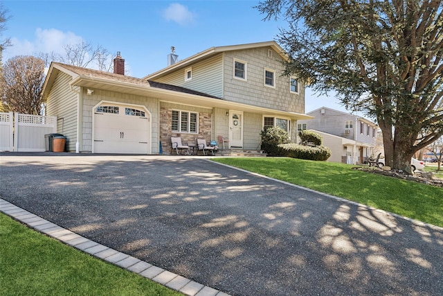 traditional-style home featuring a chimney, an attached garage, fence, driveway, and a front lawn