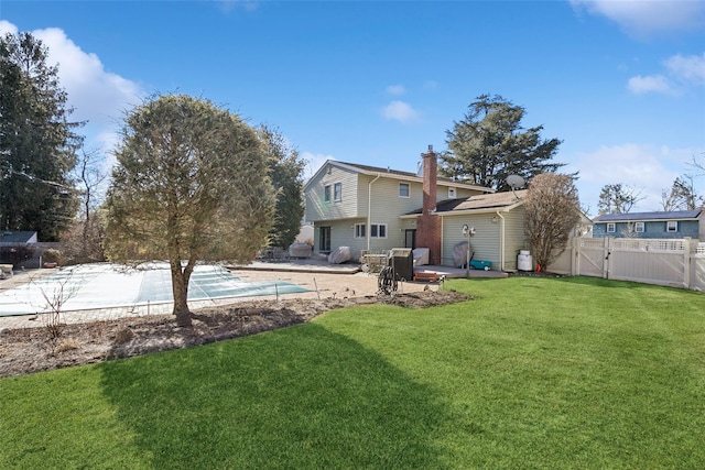 back of property featuring a gate, fence, a lawn, and a patio