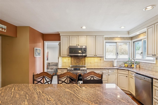 kitchen with light stone counters, recessed lighting, stainless steel appliances, a sink, and decorative backsplash