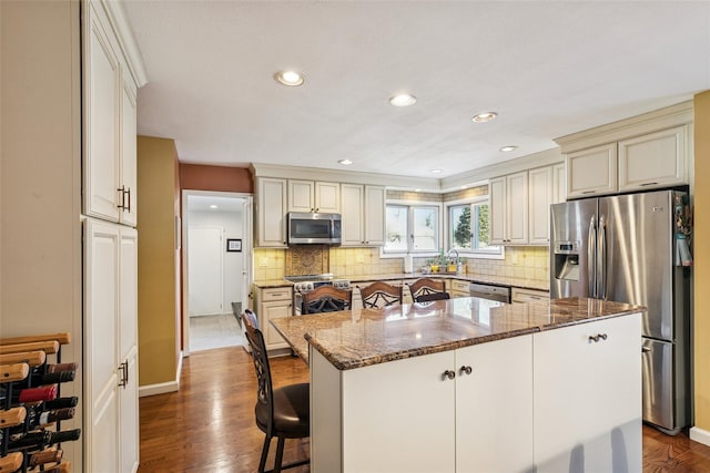 kitchen featuring dark wood-style flooring, dark stone countertops, a center island, cream cabinets, and stainless steel appliances