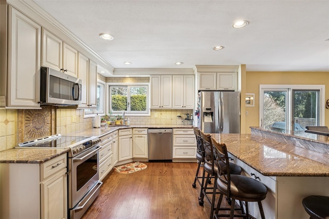 kitchen featuring wood finished floors, appliances with stainless steel finishes, a kitchen bar, and a healthy amount of sunlight