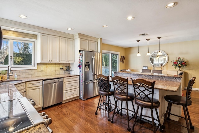 kitchen featuring visible vents, appliances with stainless steel finishes, dark wood-type flooring, a sink, and a kitchen bar