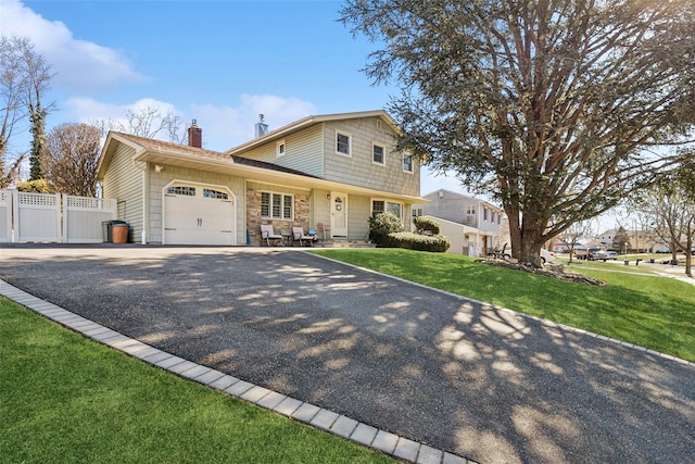 traditional-style house featuring a garage, fence, driveway, stone siding, and a front yard