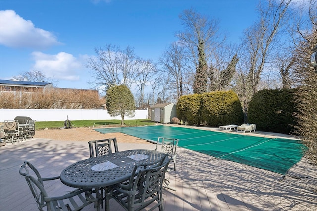 view of pool featuring an outbuilding, a fenced backyard, a fenced in pool, outdoor dining space, and a patio area