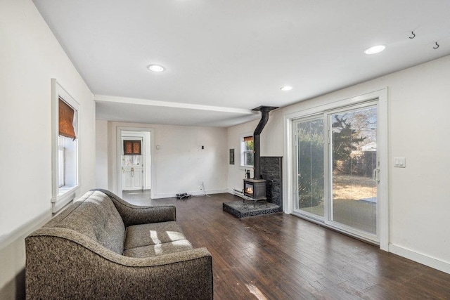 living room featuring recessed lighting, a wood stove, baseboards, and wood finished floors