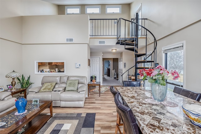 living room featuring visible vents, light wood-style flooring, a high ceiling, and stairs