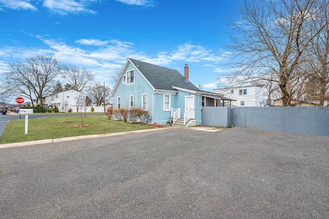 view of front facade with a chimney, stucco siding, fence, driveway, and a front lawn