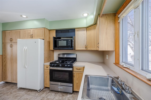 kitchen with light countertops, freestanding refrigerator, a sink, stainless steel gas range, and black microwave