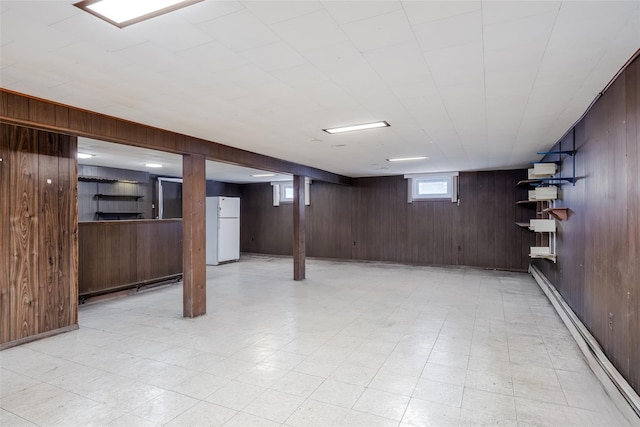 below grade area with wooden walls, freestanding refrigerator, baseboard heating, and light floors