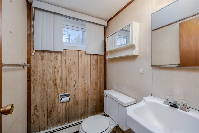 half bathroom featuring toilet, wood walls, a baseboard radiator, and a sink