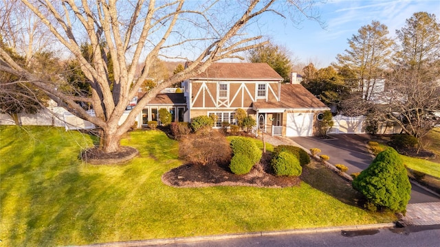 tudor house with a garage, driveway, a chimney, fence, and a front lawn