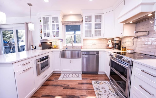 kitchen with stainless steel appliances, a peninsula, a sink, white cabinetry, and custom exhaust hood