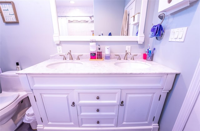 bathroom with a sink, toilet, and double vanity