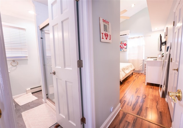 corridor featuring a baseboard heating unit, a wall unit AC, light wood-style flooring, and baseboards