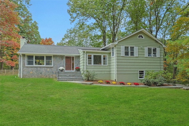 tri-level home featuring stone siding, a chimney, and a front yard