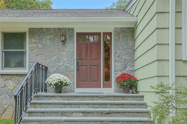 doorway to property with a shingled roof and stone siding