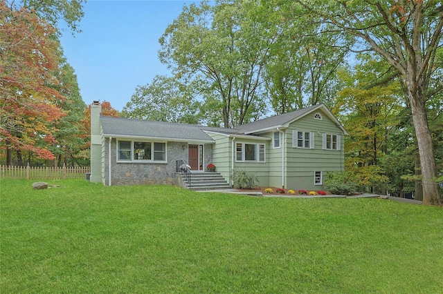 split level home with stone siding, a front lawn, a chimney, and fence