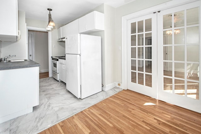 kitchen featuring under cabinet range hood, a sink, white cabinets, freestanding refrigerator, and gas range