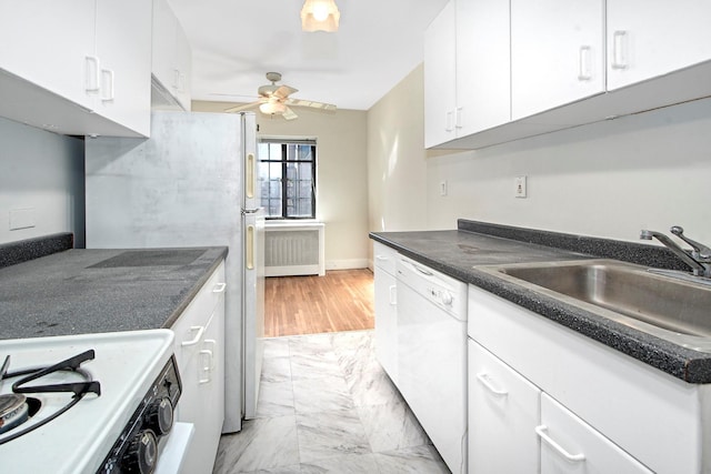 kitchen with white appliances, a sink, a ceiling fan, white cabinets, and dark countertops