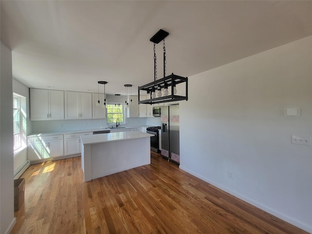 kitchen featuring a kitchen island, appliances with stainless steel finishes, hanging light fixtures, light countertops, and white cabinetry