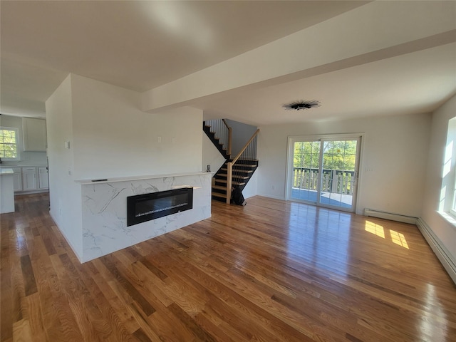 unfurnished living room featuring stairs, a premium fireplace, wood finished floors, and a healthy amount of sunlight