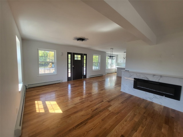 unfurnished living room with a high end fireplace, a baseboard radiator, and wood finished floors