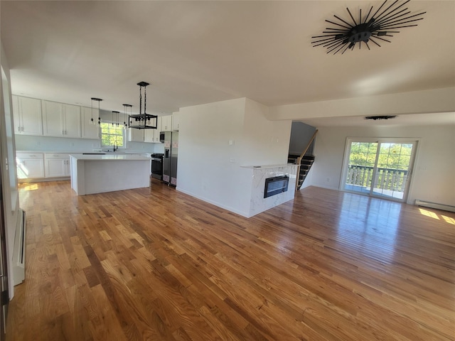 unfurnished living room with a baseboard heating unit, a sink, a glass covered fireplace, and light wood-style flooring