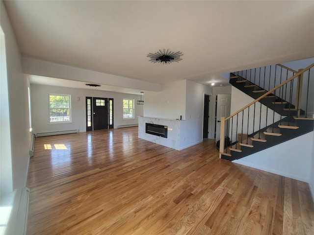 unfurnished living room featuring a baseboard radiator, wood finished floors, a high end fireplace, baseboards, and stairs